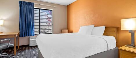 Hotelkamer met een groot bed, een bureau met stoel, een raam met blauwe gordijnen en een nachtkastje met lamp.