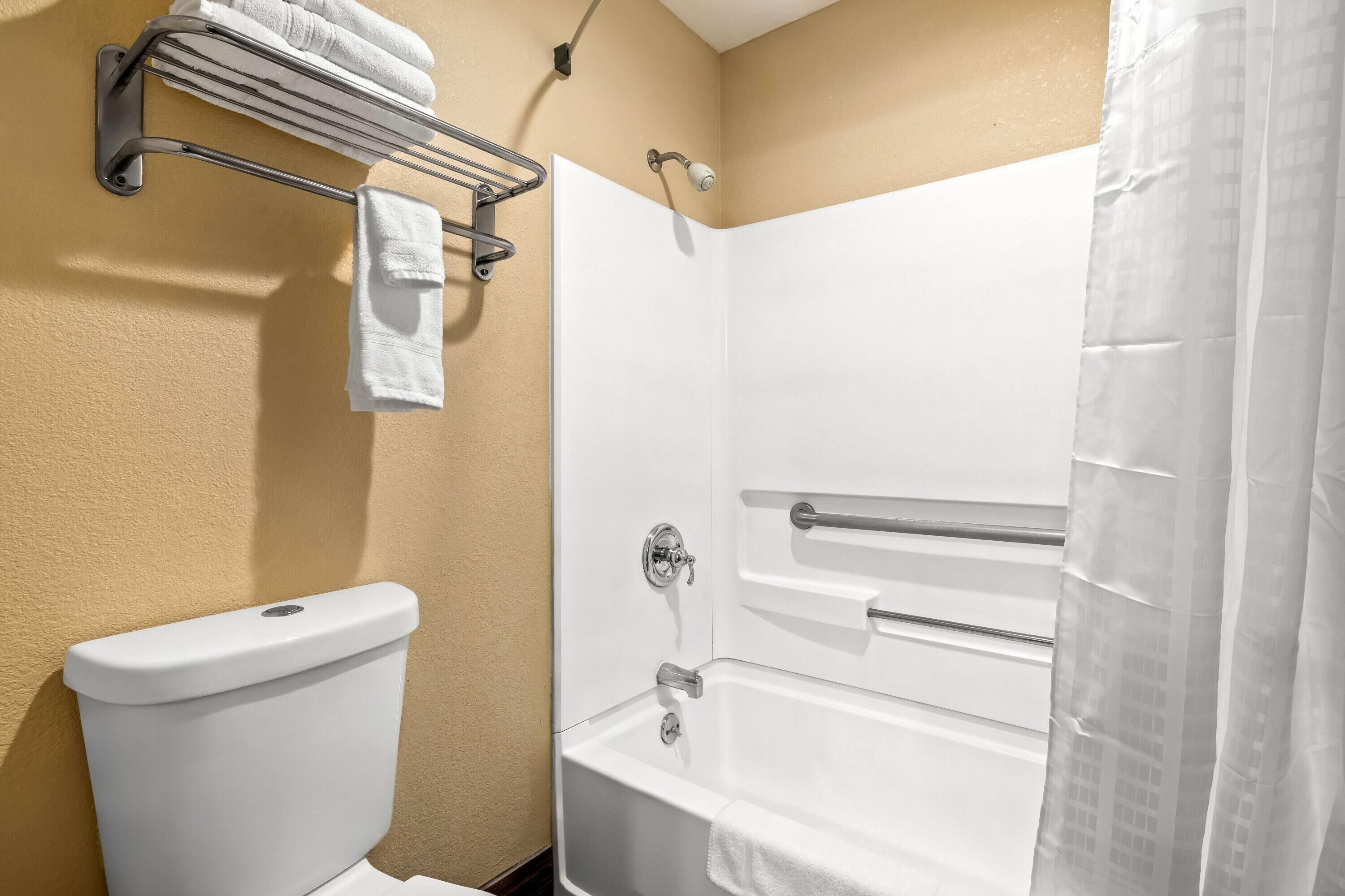 A bathroom with a white toilet, a bathtub with a shower curtain, and a towel rack with towels.
