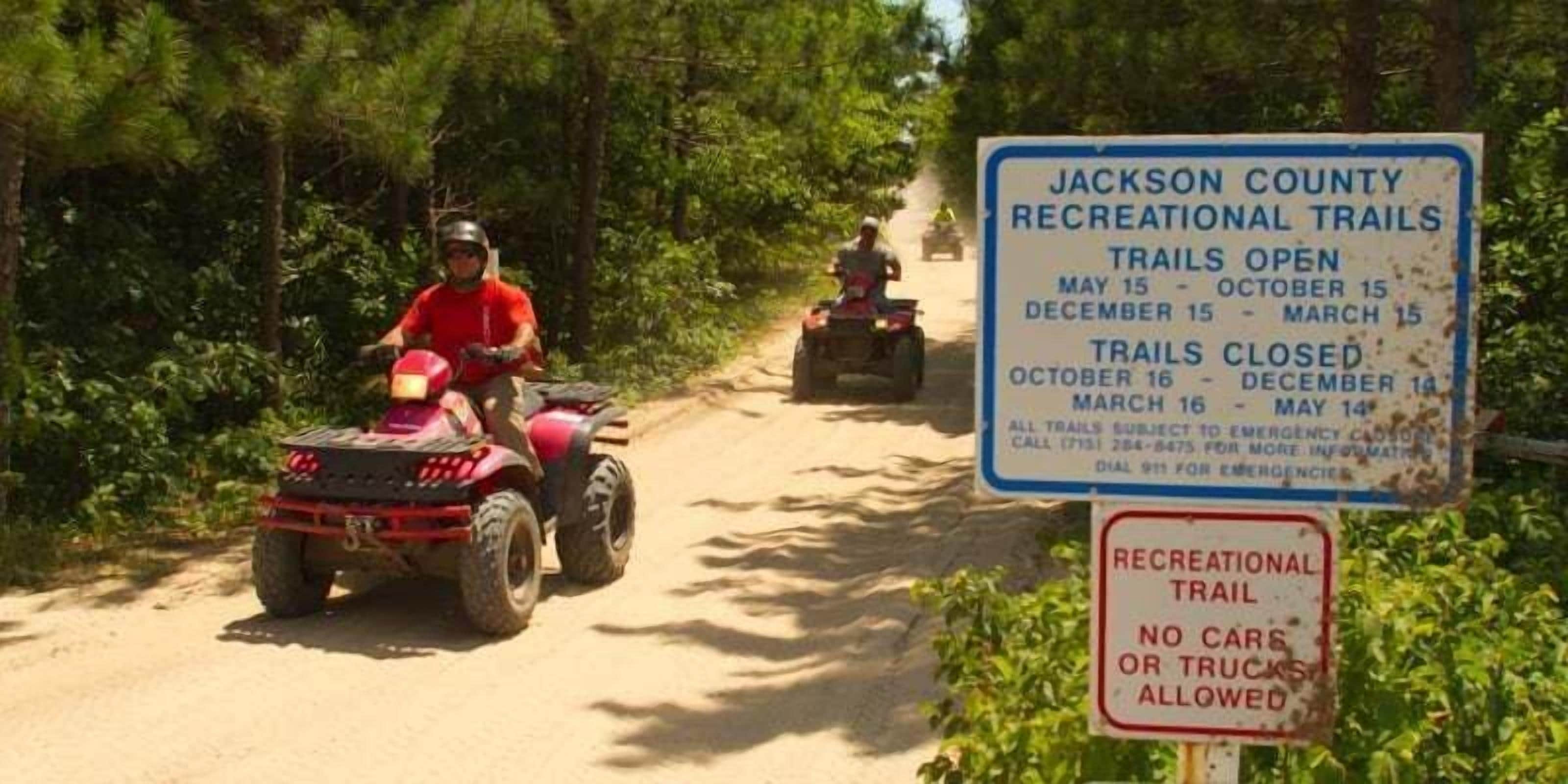 A dirt trail with ATVs and a sign indicating Jackson County Recreational Trails open from May 15 to October 15 and December 15 to March 15, with no cars or trucks allowed.