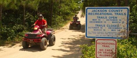 A dirt trail with ATVs and a sign indicating Jackson County Recreational Trails open from May 15 to October 15 and December 15 to March 15, with no cars or trucks allowed.
