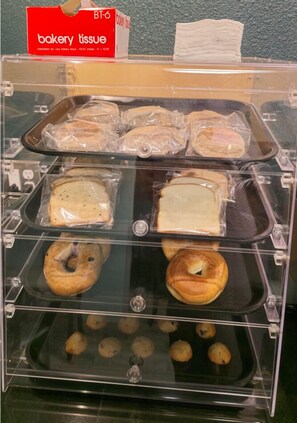 A bakery display case with various baked goods, including bread, bagels, and muffins, covered with bakery tissue.