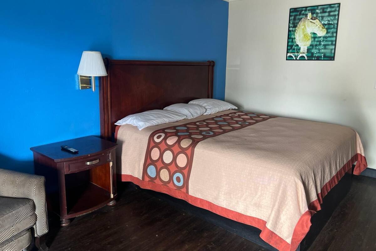 A hotel room with a wooden bed, a nightstand, a lamp, and a wall painting.