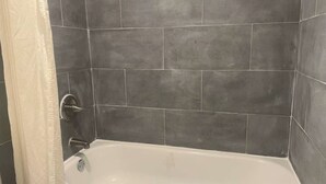 A bathroom with a white bathtub, dark grey tiles, and a white shower curtain. - Capitol Inn by Belvilla Richmond Airport VA (Sandston)