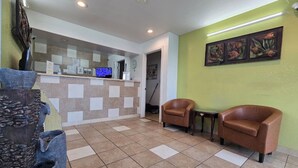 A reception area with a check-in counter, two leather chairs, a stone fountain, and artwork on the wall. - Capitol Inn by Belvilla Richmond Airport VA (Sandston)