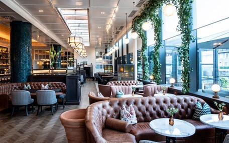 Un amplio salón con sofás de cuero, mesas redondas y una zona de bar con estanterías.