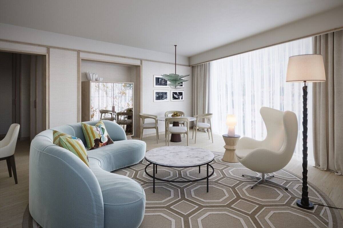 Une chambre d’hôtel moderne avec un canapé bleu clair, une table basse ronde, un fauteuil blanc et un lampadaire.