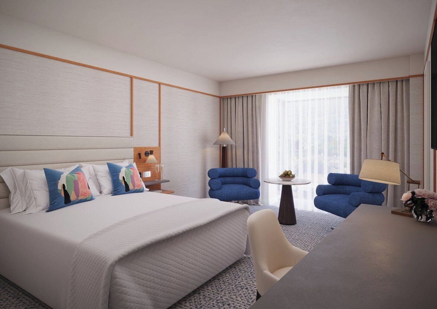 A hotel room with a large bed, two blue armchairs, a small round table, and a desk with a lamp.