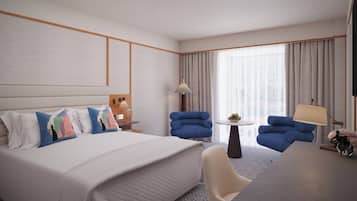 A hotel room with a large bed, two blue armchairs, a small round table, and a desk with a lamp.