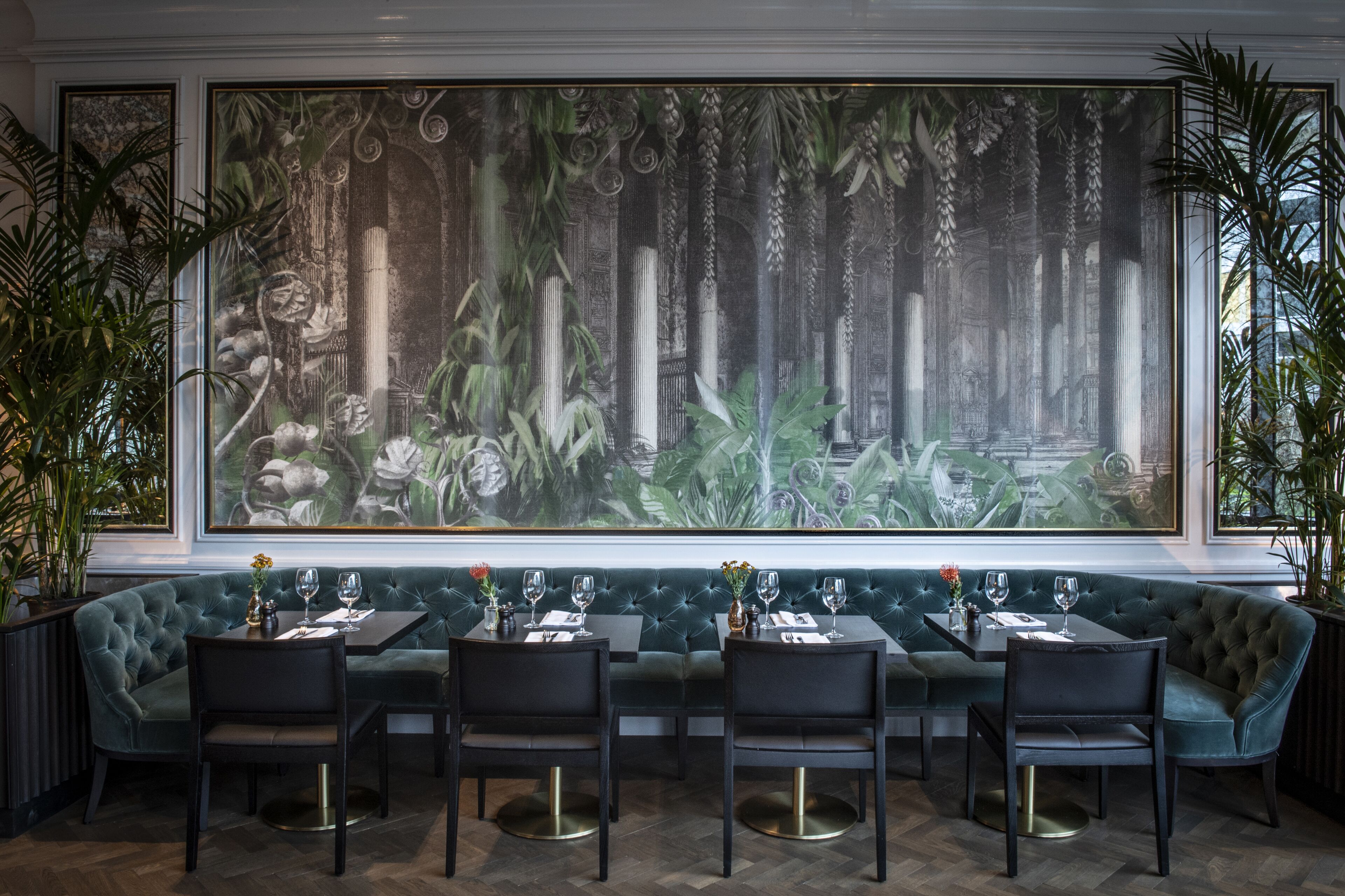 Un restaurant orné d’une grande fresque représentant une scène de jungle, avec des sièges rembourrés de tissu vert et des chaises noires.