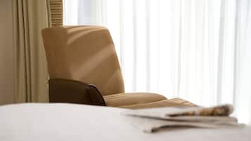 Una habitación de hotel con cama, una silla y ventana con cortinas traslúcidas.