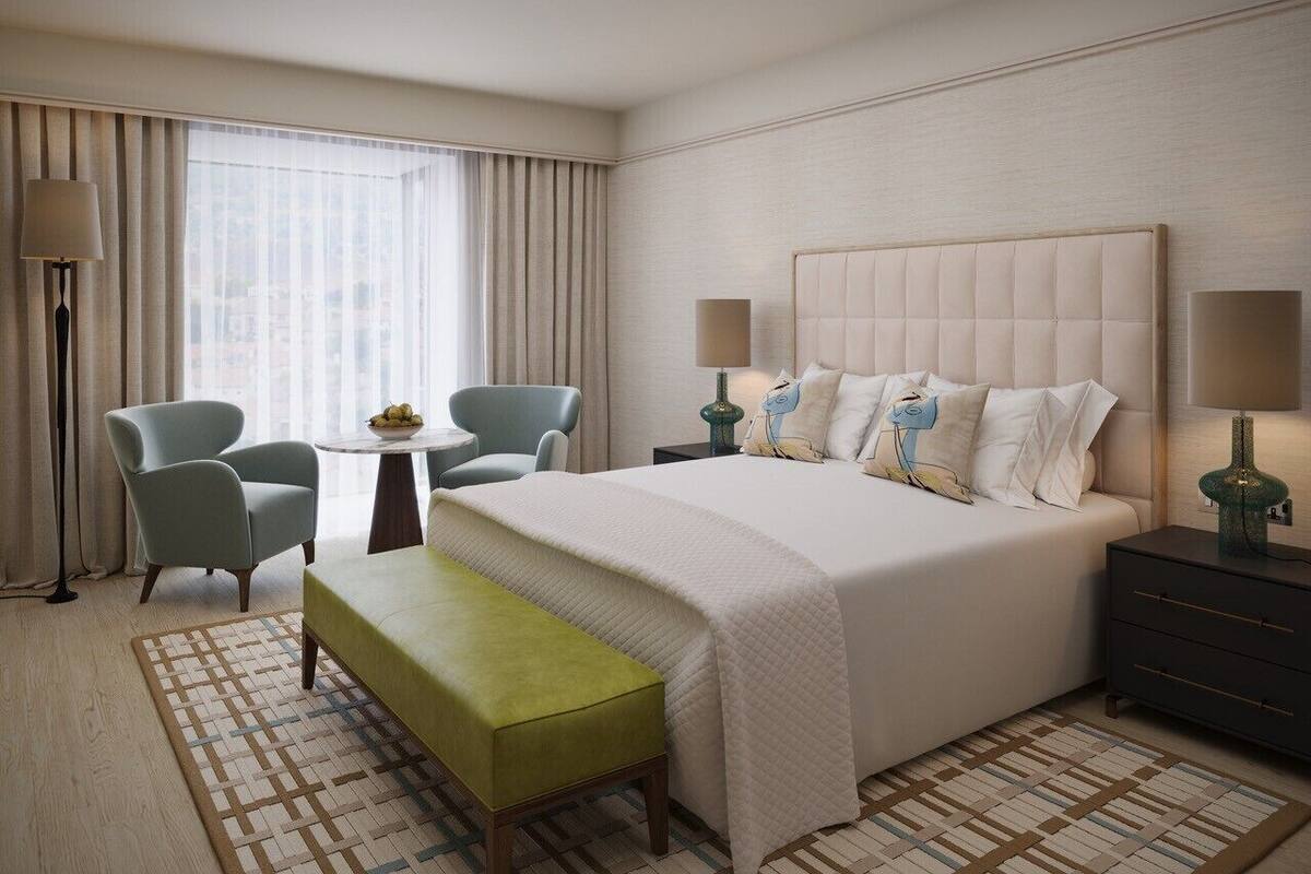 Une chambre d’hôtel comprenant un lit, deux chaises, une petite table, un banc et une table de chevet avec des lampes.
