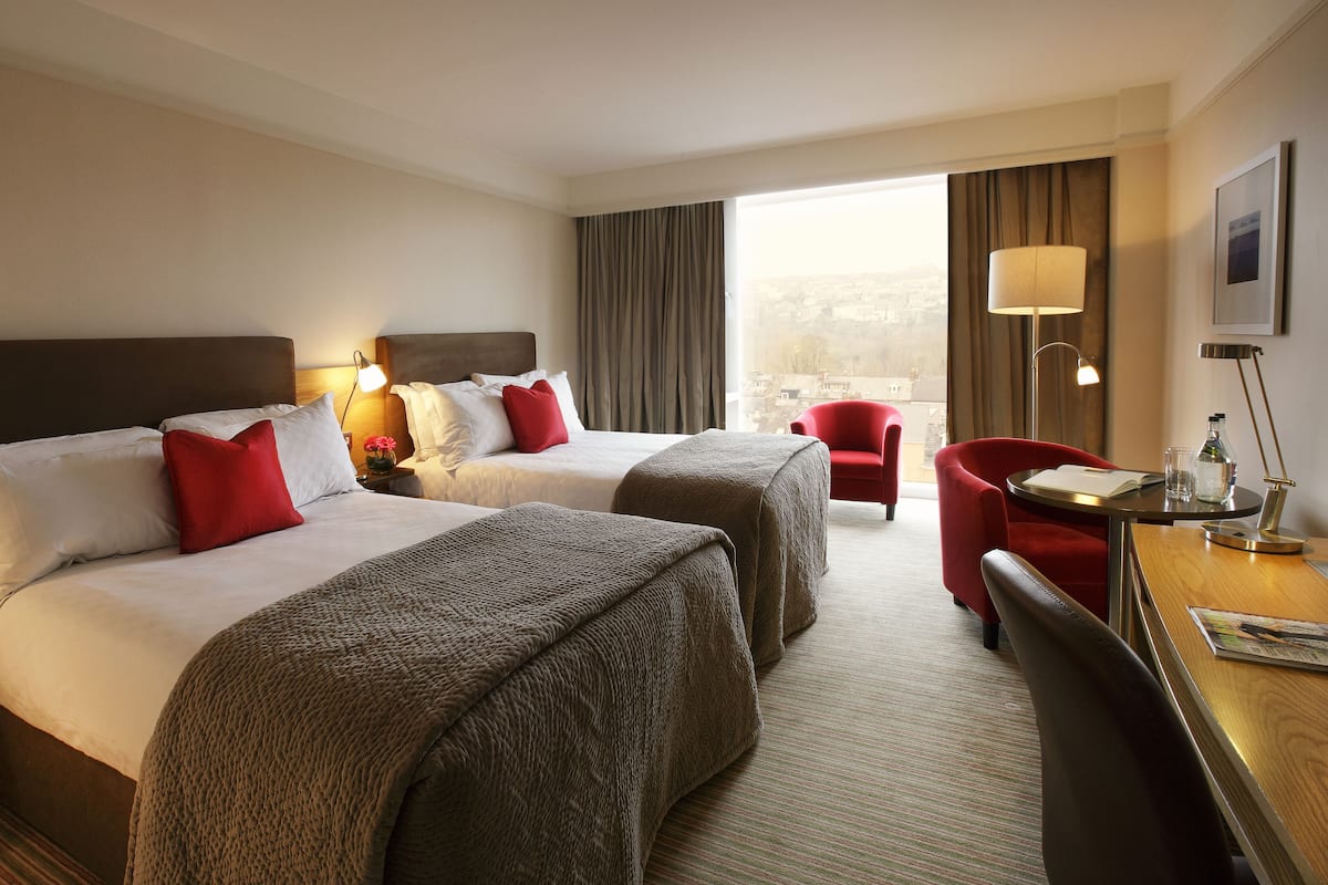 Une chambre d’hôtel avec deux lits, un bureau, une chaise et une vue sur la ville.
