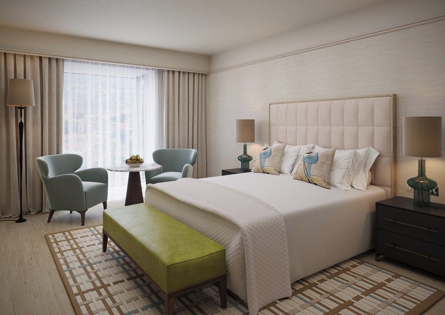 Une chambre d’hôtel avec un grand lit, deux fauteuils, une petite table sur laquelle se trouve un saladier de fruits, un banc et une table de chevet avec une lampe.