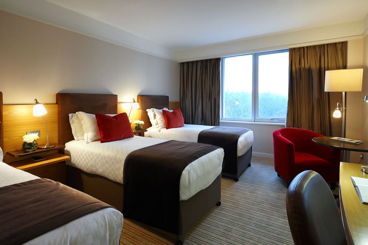 Une chambre d’hôtel avec deux lits, un bureau, une chaise et une fenêtre avec des rideaux.