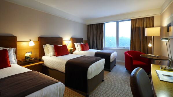 A hotel room with two beds, a desk, a chair, and a window with curtains.