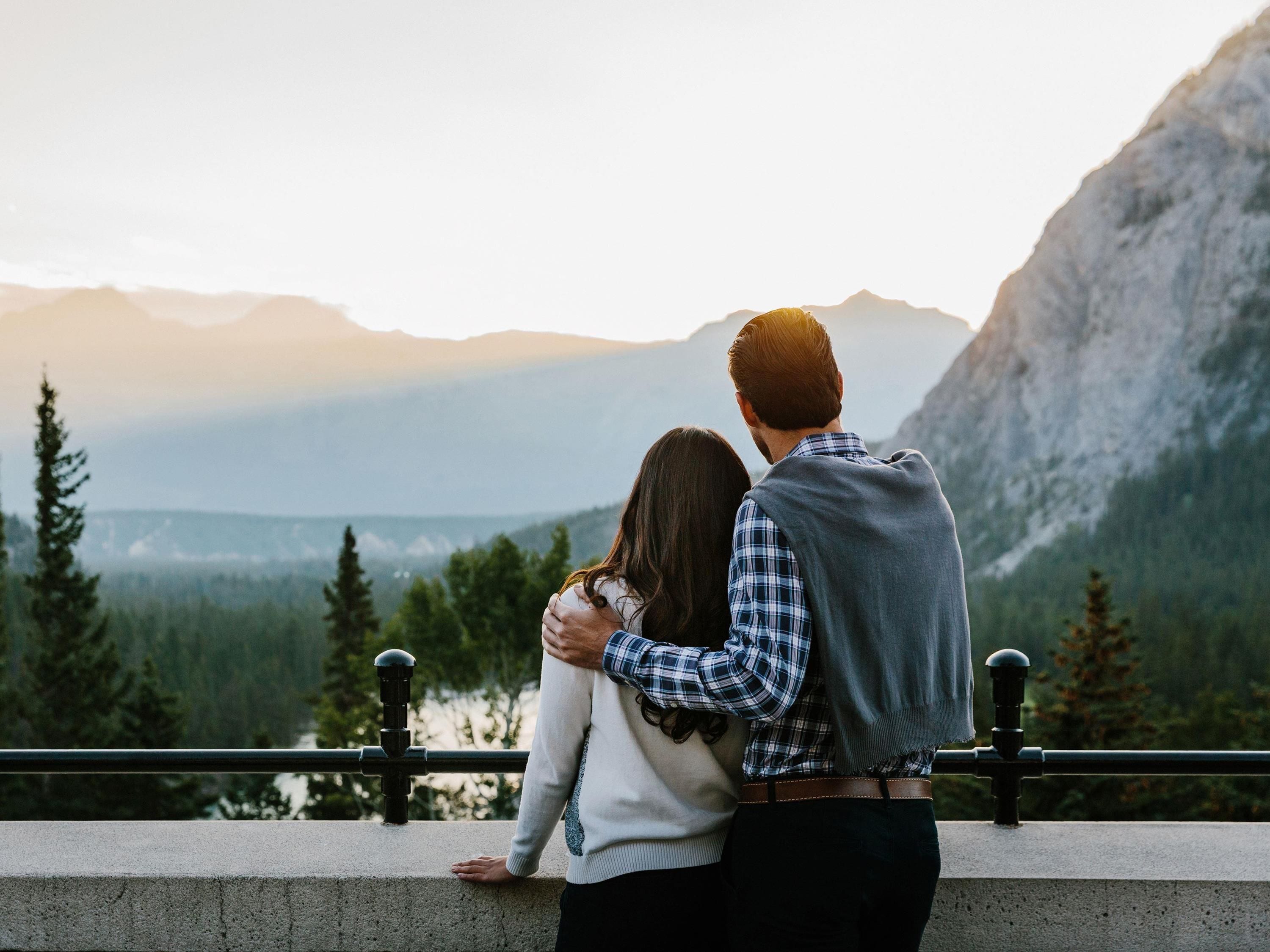 A couple embracing on a balcony overlooking a mountainous landscape.