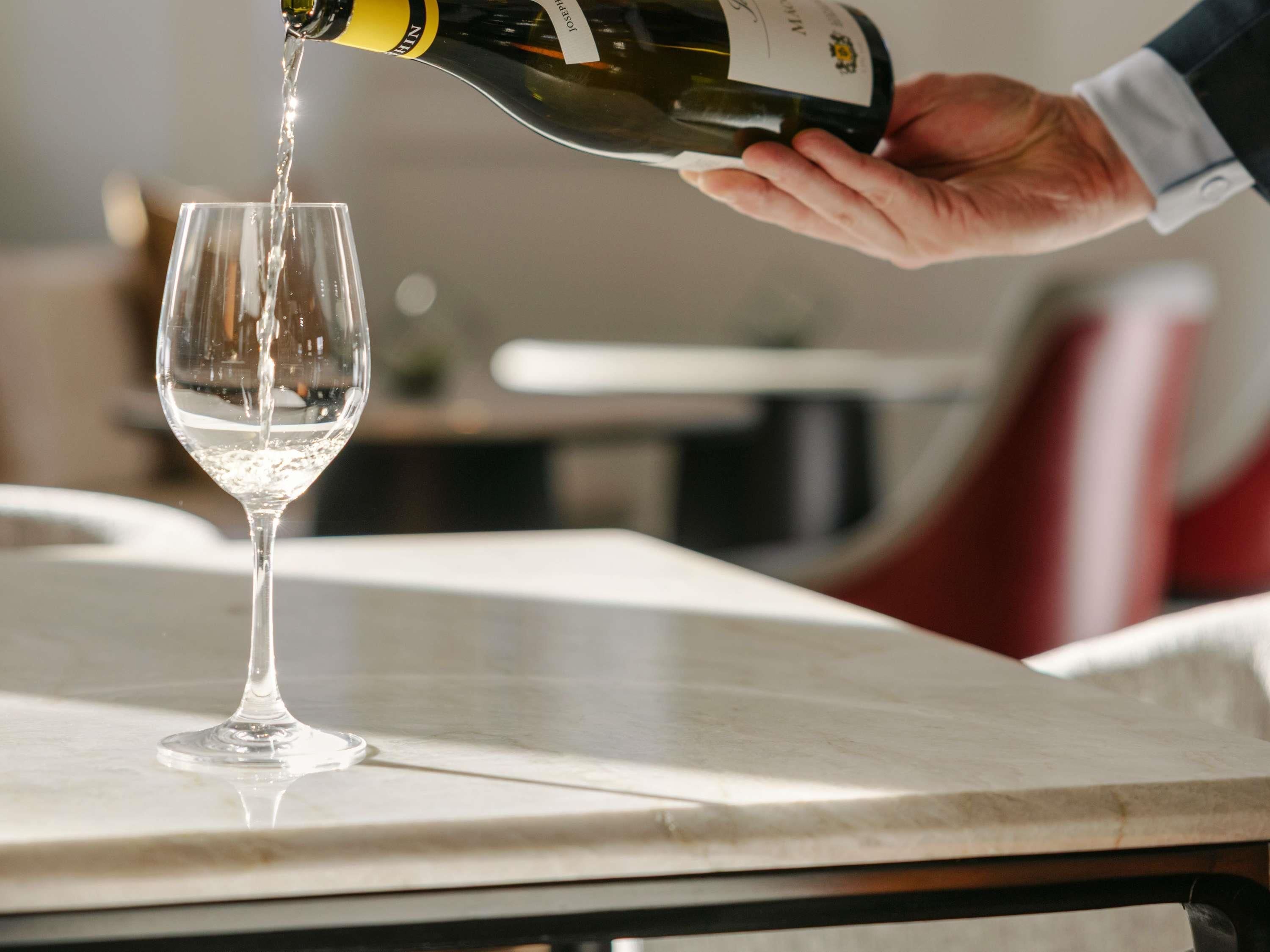 A hand pouring wine into a glass on a marble table.