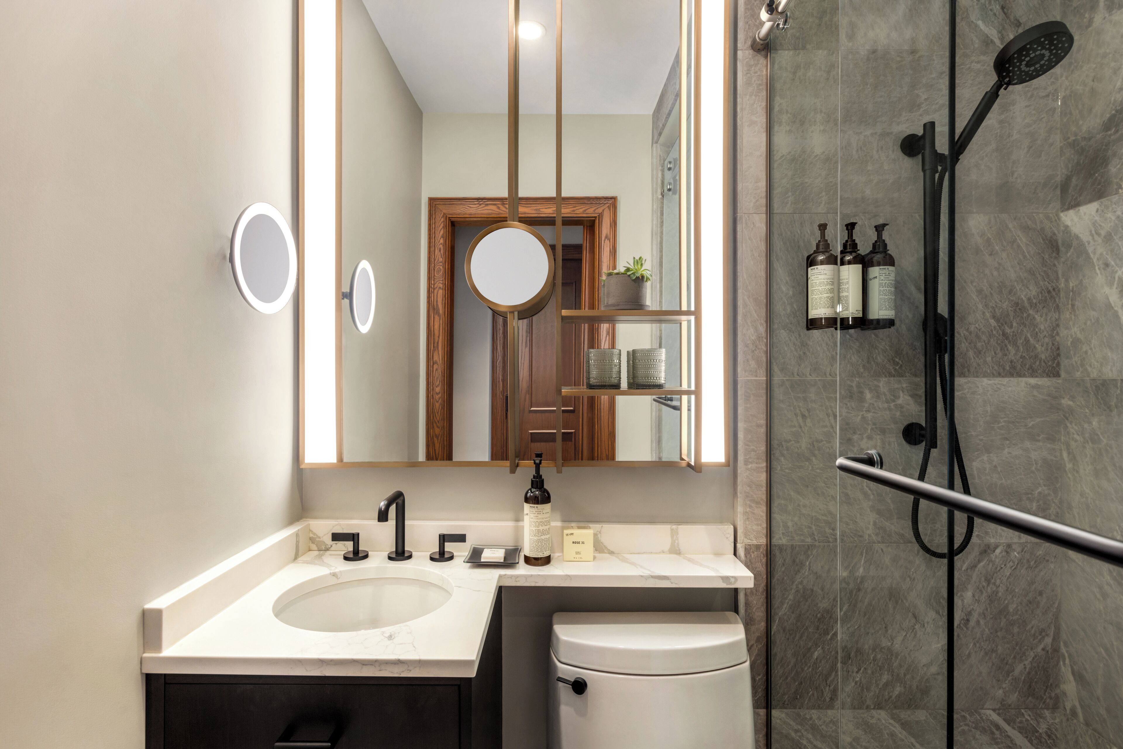 A modern bathroom with a double sink, a toilet, a mirror, and a shower area.
