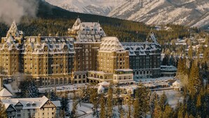 A large, historic hotel with multiple buildings, surrounded by snow-covered mountains and trees.