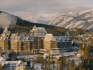 Un hotel grande e histórico con varias edificaciones, rodeado de montañas y árboles cubiertos de nieve.
