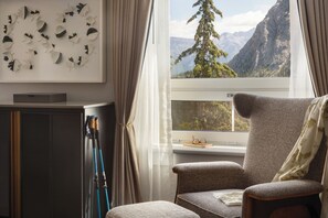 A room with a view of mountains, a chair, a table with glasses, and a wall with leaf art.