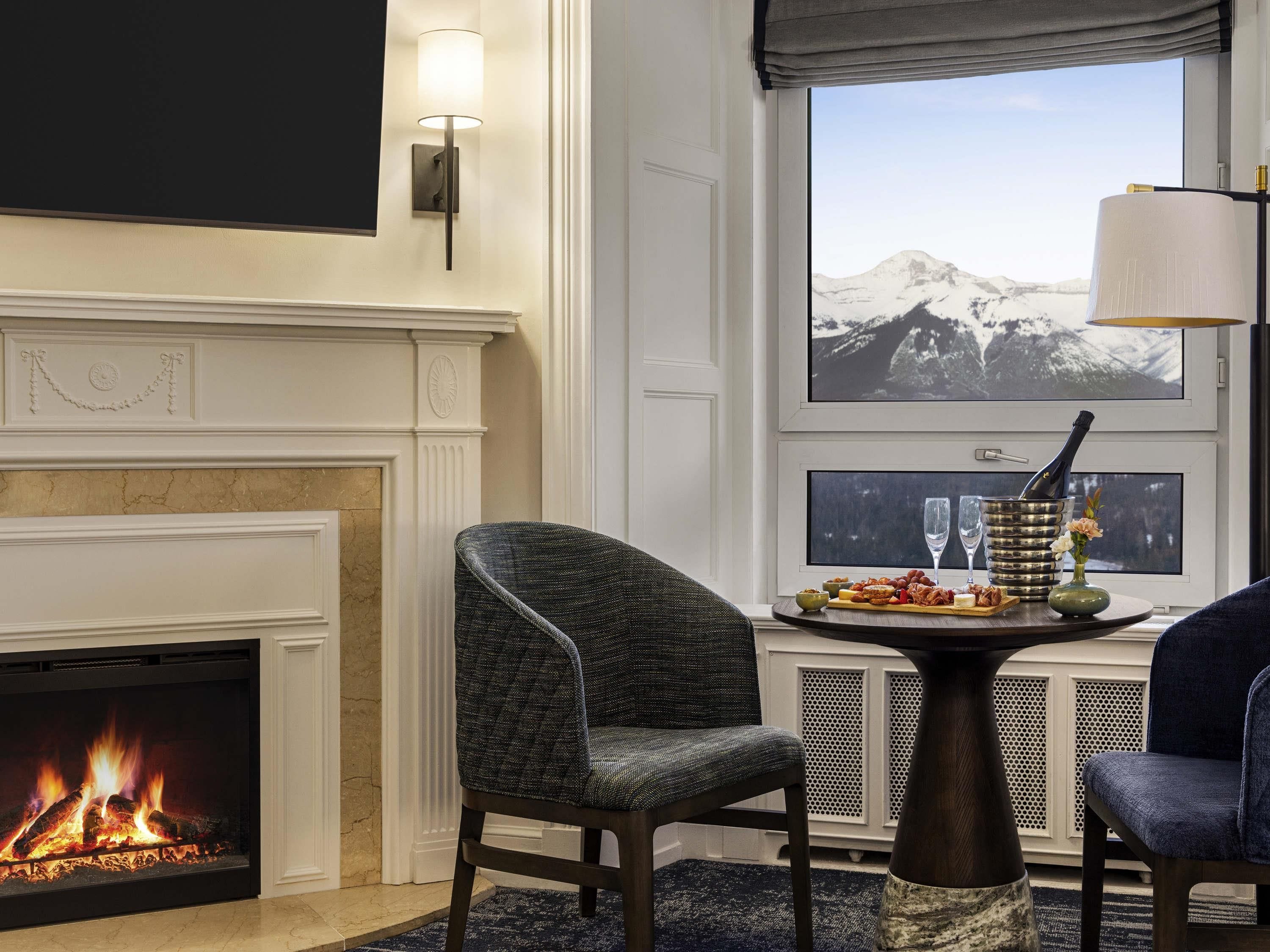 A room with a fireplace, a dining table with chairs, a window with a mountain view, and a wall-mounted lamp.