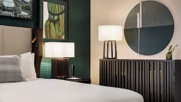 A modern hotel room with a bed, two bedside lamps, a round mirror, and a decorative plant.