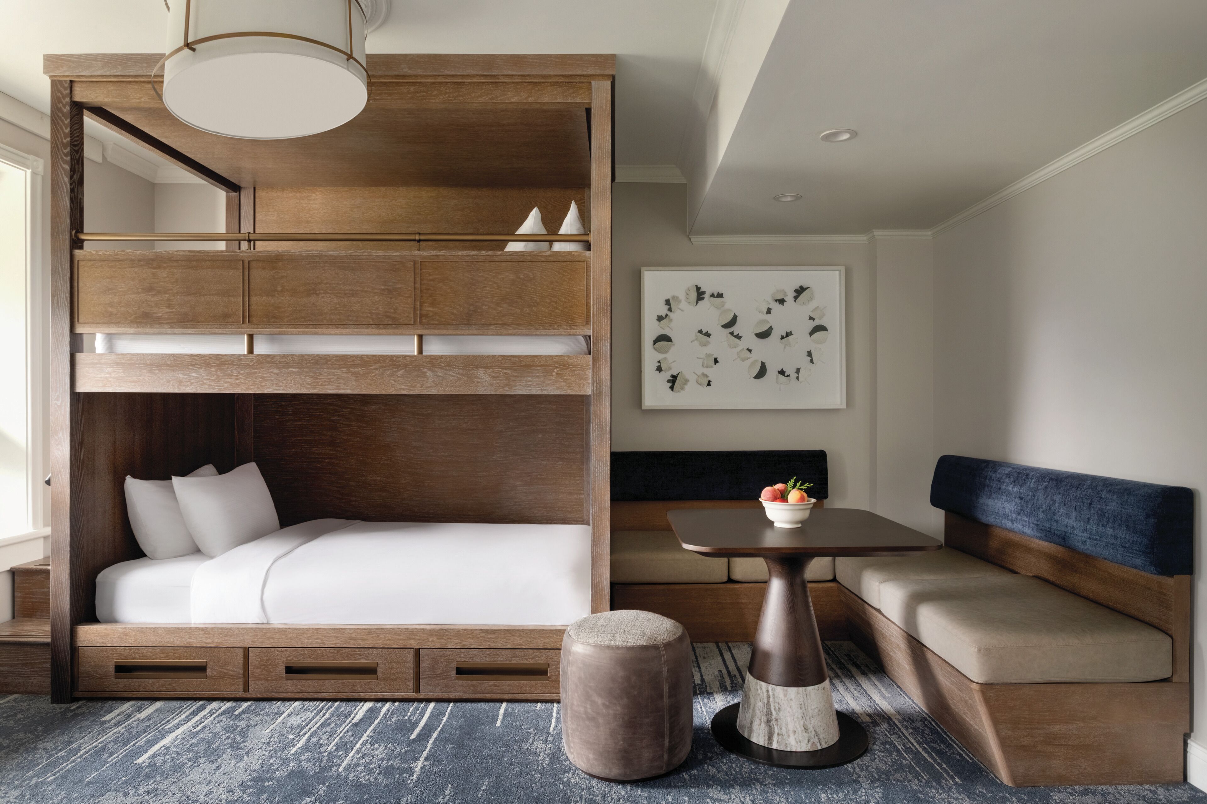 Quarto moderno com beliche, sofá, mesinha com uma tigela de fruta e um objeto decorativo na parede.