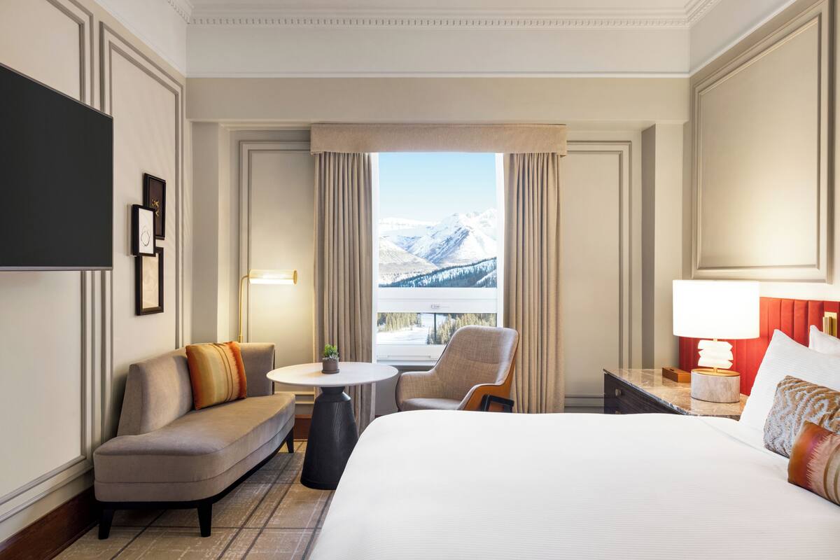 A hotel room with a large bed, a sofa, a chair, a small table, and a TV.