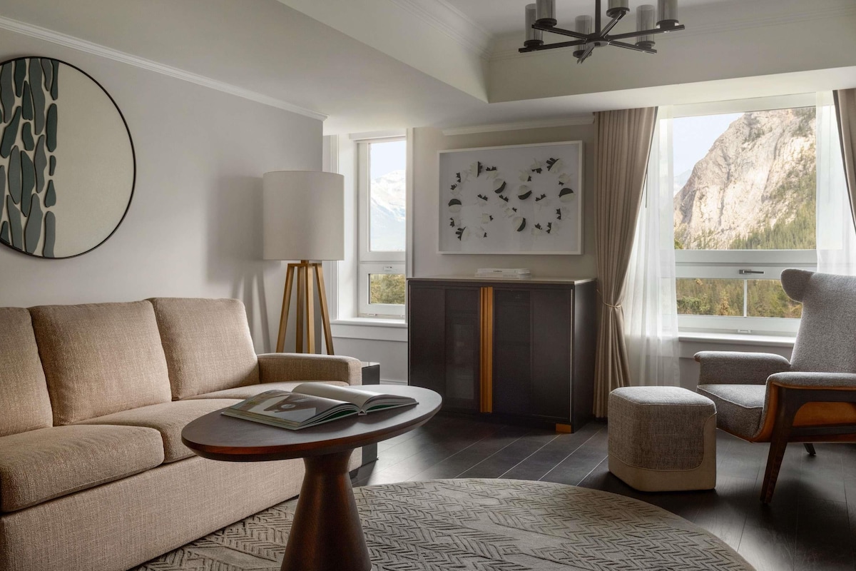 A modern living room with a sofa, a coffee table, a lamp, a fireplace, and a view of a mountain.