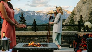 A terrace with a stone fireplace, a telescope, and a mountainous backdrop.
