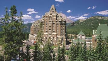 A large, historic hotel with a prominent tower, surrounded by dense forest and mountains.