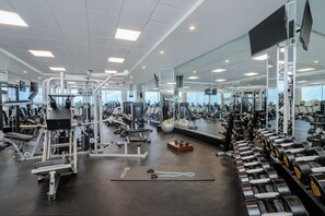 A gym with various exercise equipment, mirrors, and a large window.
