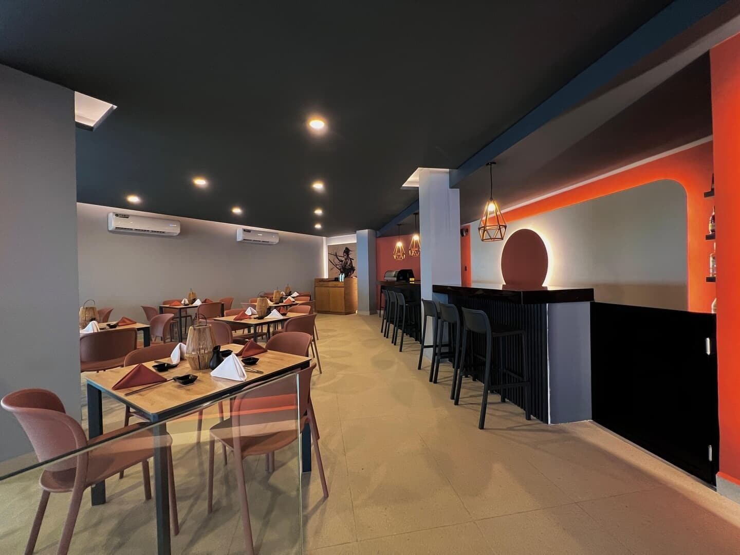 Un restaurante moderno con una barra larga, varias mesas y sillas.