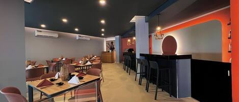 Un restaurante moderno con una barra larga, varias mesas y sillas.
