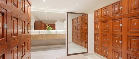A hotel lobby with wooden lockers numbered from 1 to 12, a bench, and a mirror reflecting the lockers.