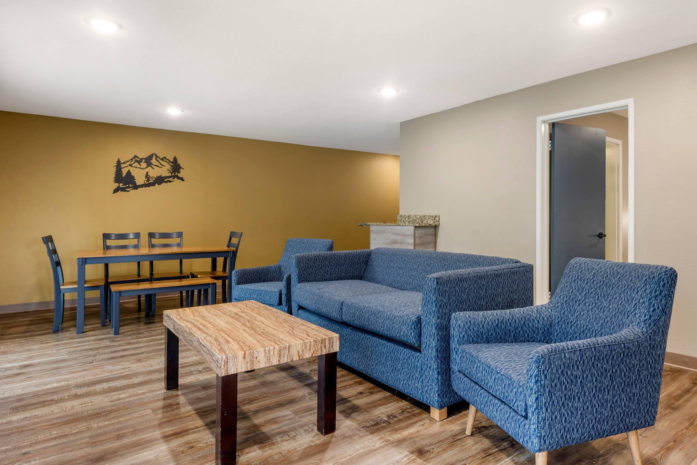 Een woonkamer met een houten salontafel, blauwe gestreepte banken, een eettafel met stoelen en een aan de muur hangend kunstwerk.