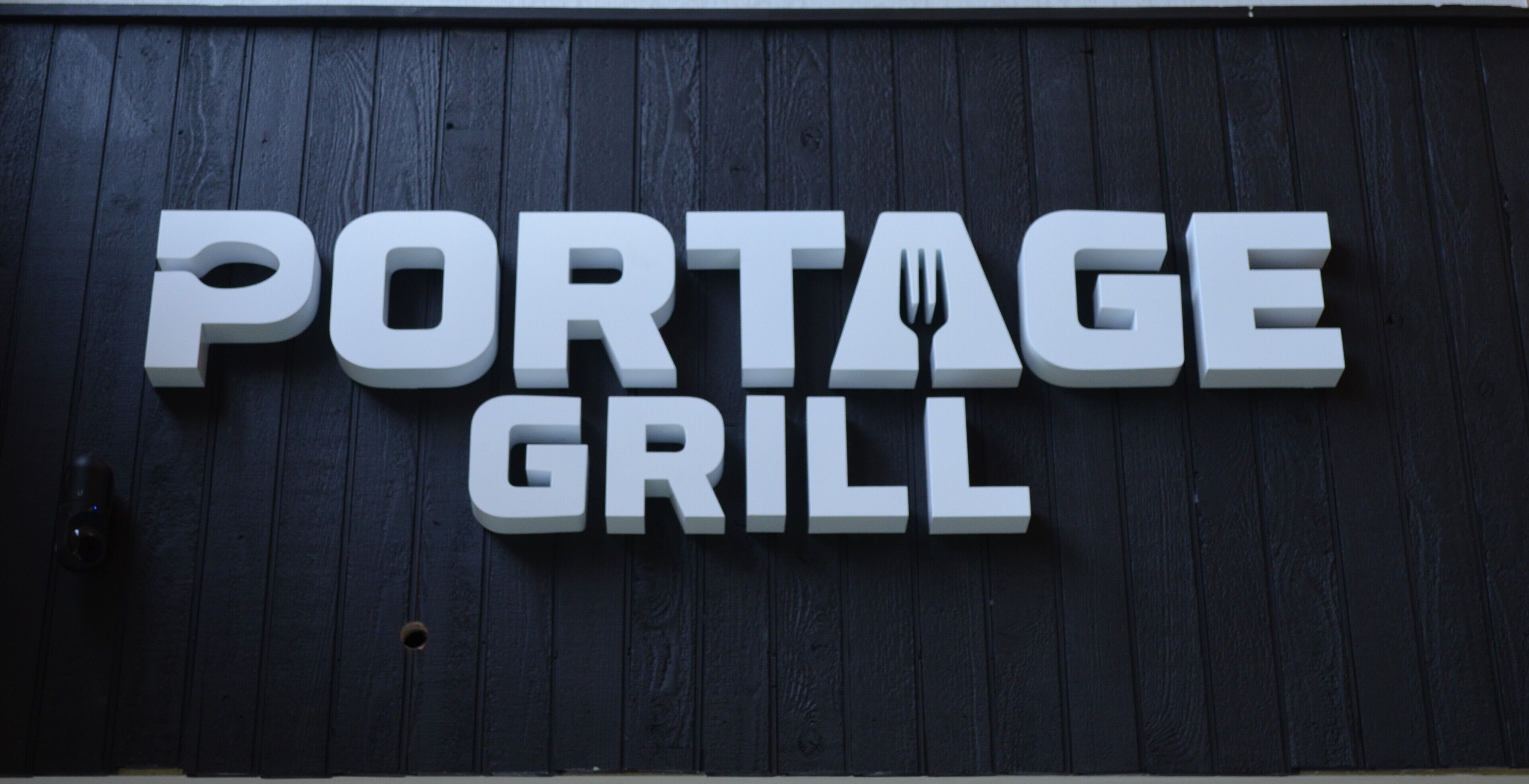 Letrero de 'PORTAGE GRILL' sobre una pared de madera oscura.