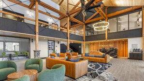 A spacious lobby with high ceilings, wooden beams, and a large chandelier. There are multiple seating areas with sofas and armchairs. A reception desk is visible in the background. - Columbia River Hotel and Conference Center, an Ascend Collection Hotel (The Dalles)