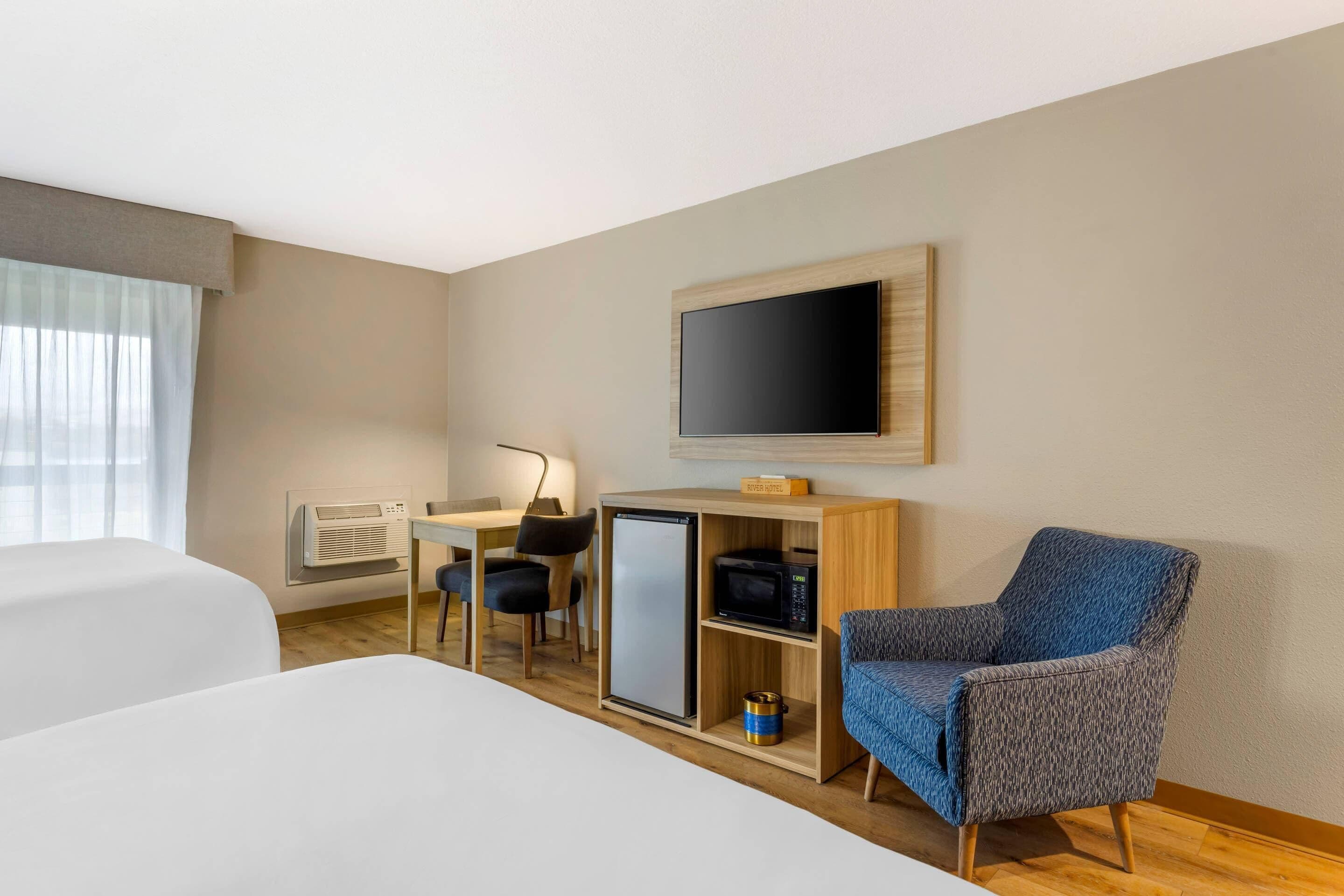 Een hotelkamer met een bed, een bureau met een computer, een televisie, een magnetron en een stoel.