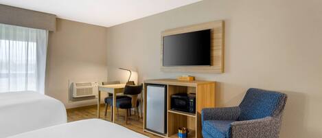 Een hotelkamer met een bed, een bureau met een computer, een televisie, een magnetron en een stoel.