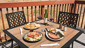 Une table en bois, dressée sur un balcon avec vue sur une jetée et l’eau, porte un repas composé d’une salade, de viande rôtie et de pain.