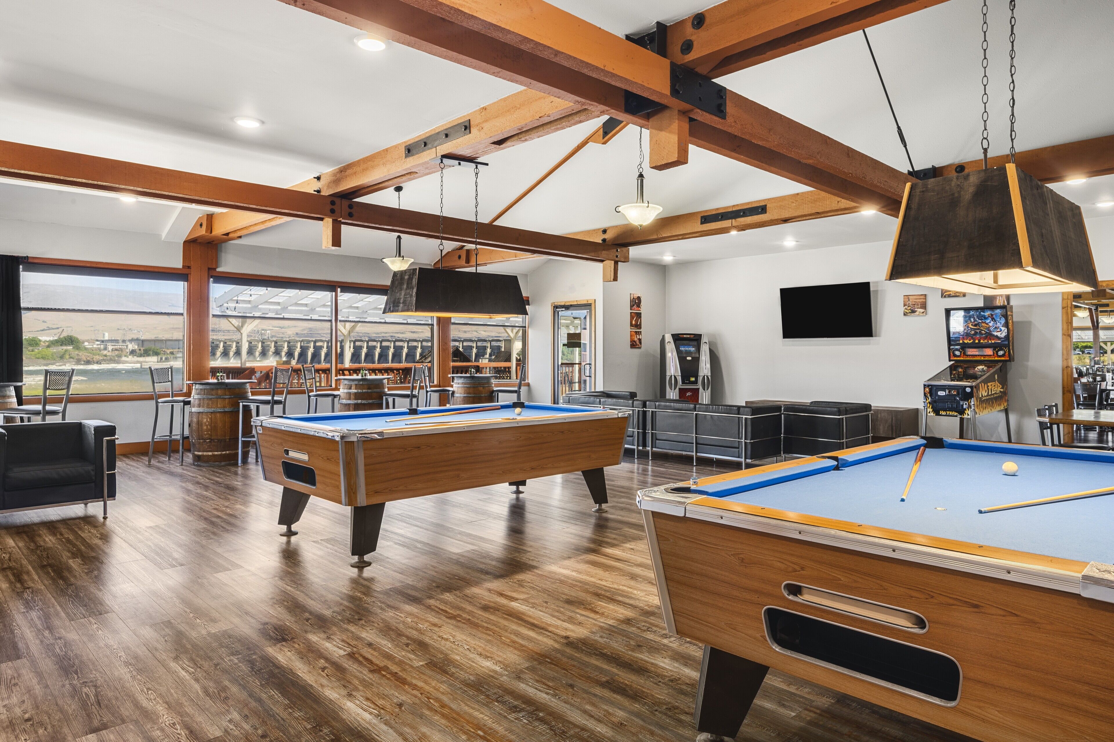 A pool table in a room with wooden beams and large windows.