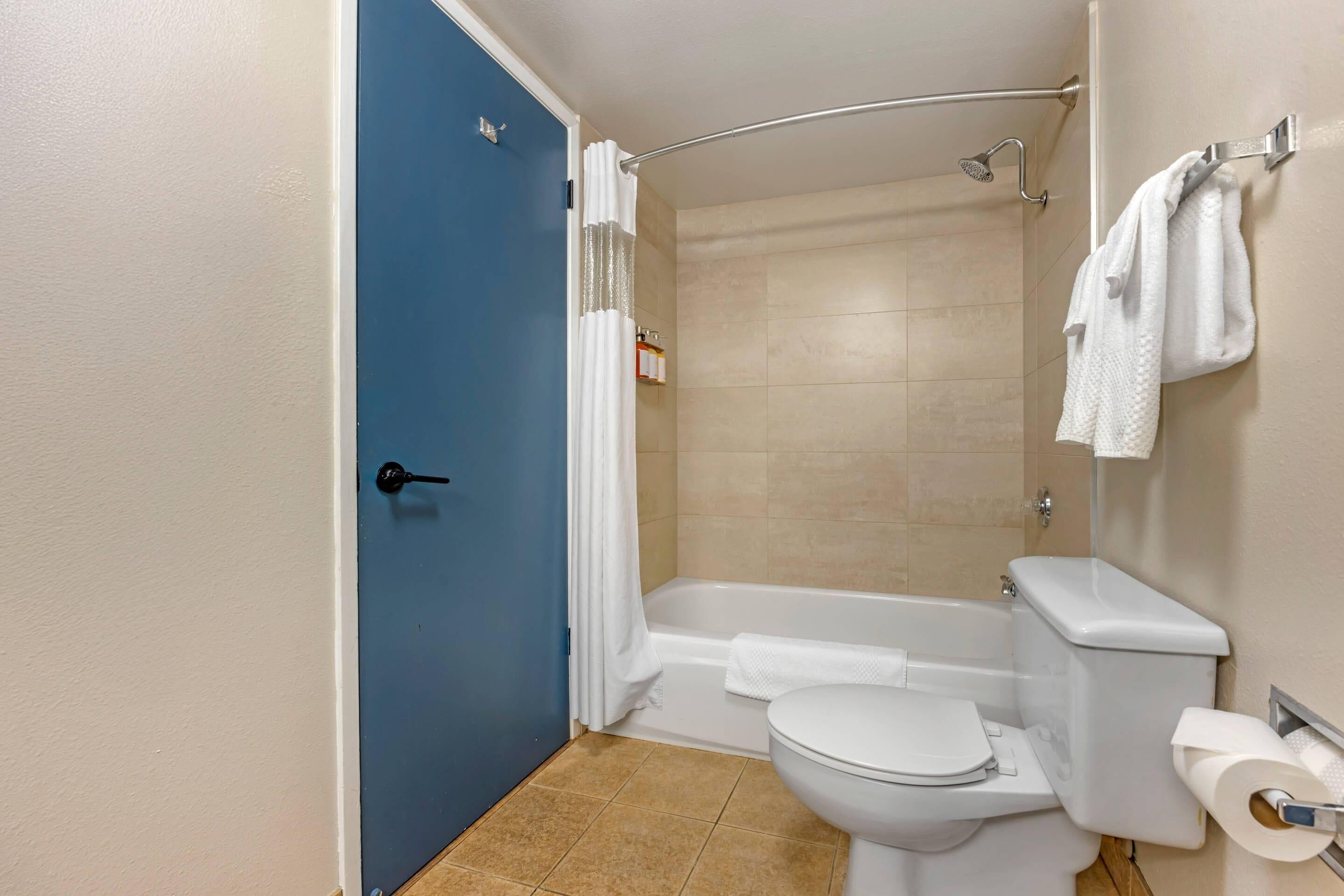 A bathroom with a blue door, a white toilet, a bathtub, and a shower.