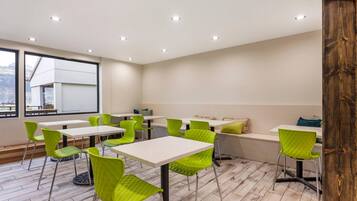 A modern dining area with white tables and green chairs, large windows, and a view of the city.