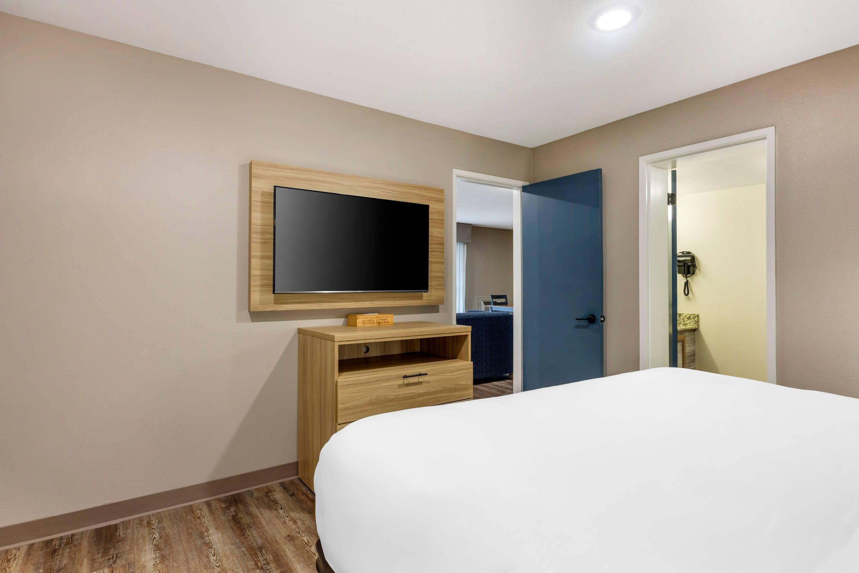 A hotel room with a bed, a TV on a wooden stand, a door, and a mirror.