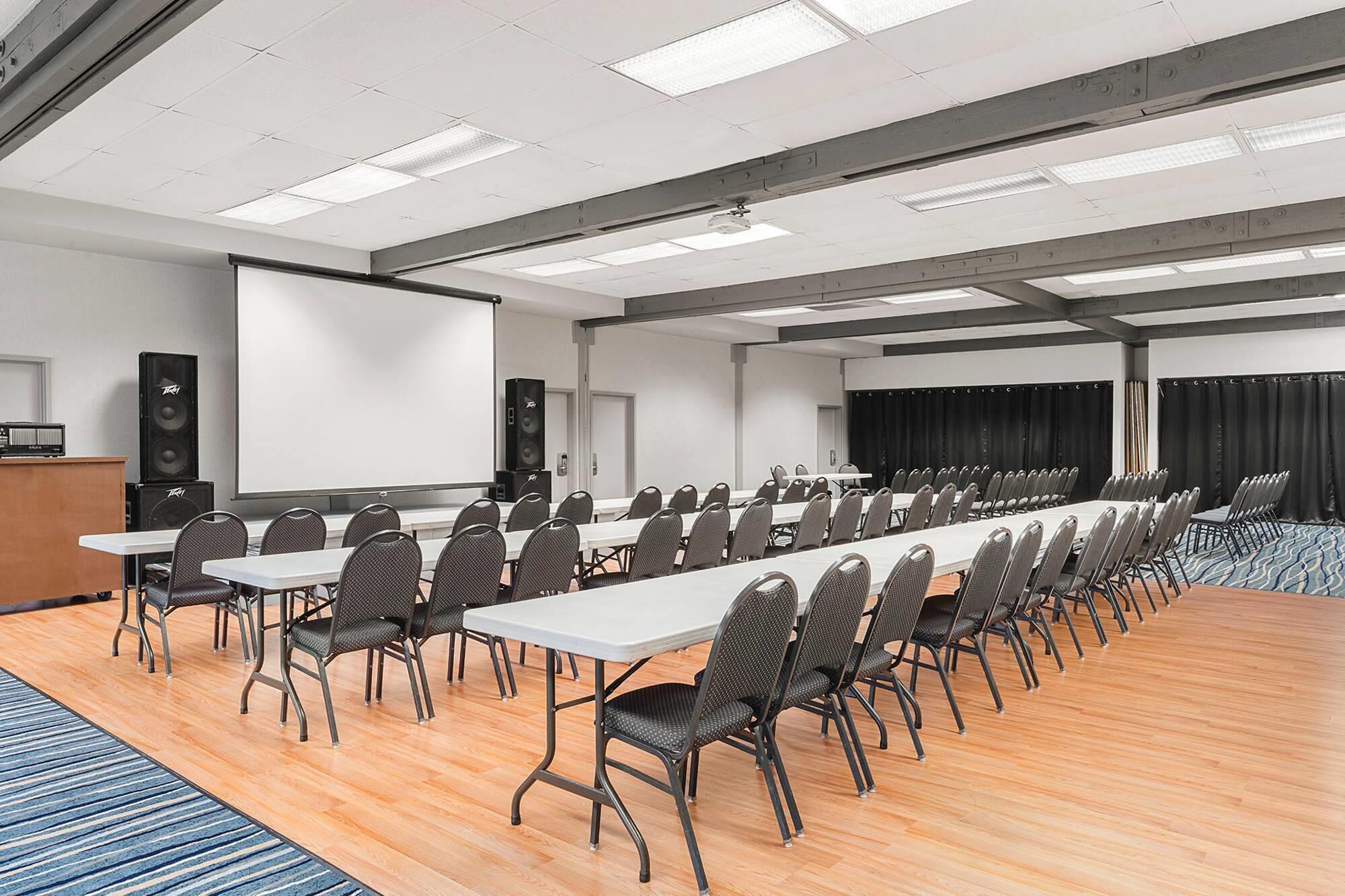 A conference room with a long table, chairs, a projector screen, and speakers.