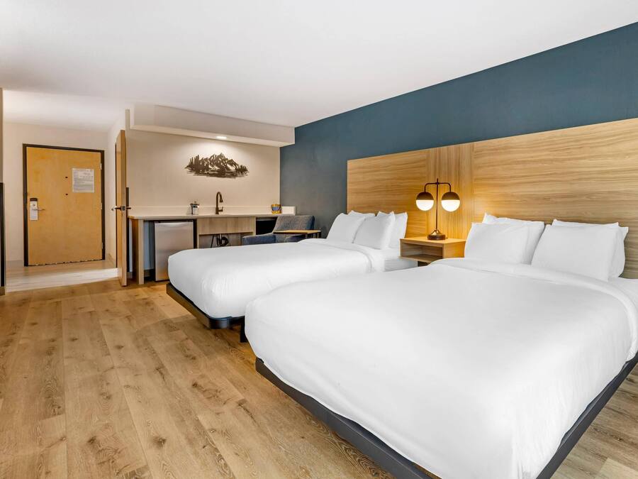 Habitación de hotel con dos camas, un escritorio, una silla, una lámpara y cabecero de madera.