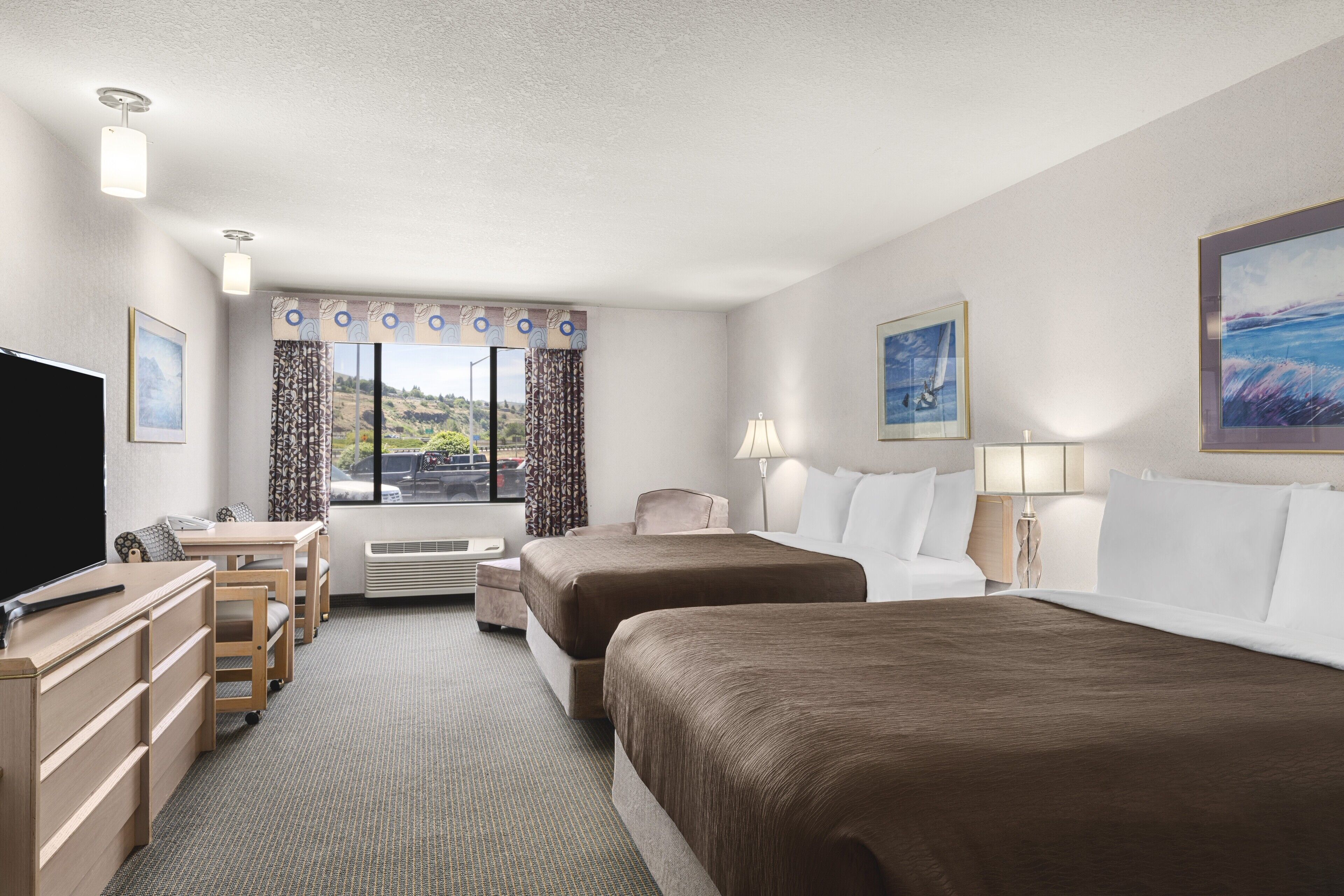 A hotel room with two beds, a desk, a TV, and a window with curtains.