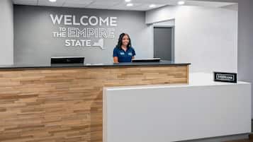 A reception desk with a 'WELCOME TO THE EMPIRE STATE' sign, a laptop, and a 'Hilton Honors' sign.